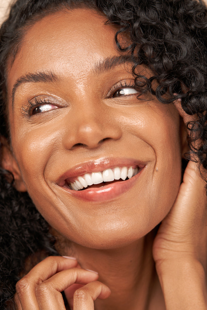 Close-up of a smiling woman with curly hair and glowing skin