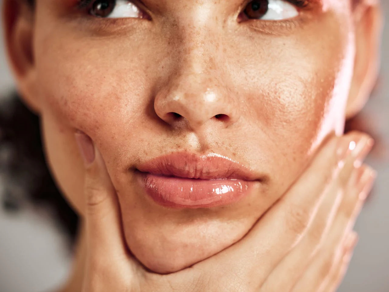 Close-up of freckled skin and glossy lips, a hand resting against the cheek