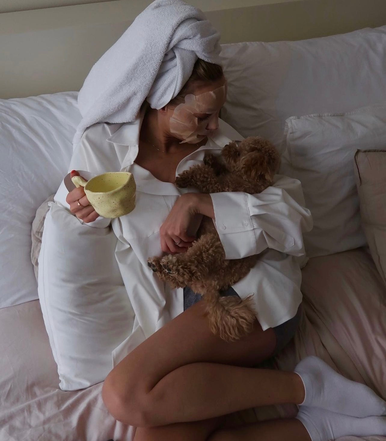 Woman relaxing with a hair towel and face mask, holding her dogs