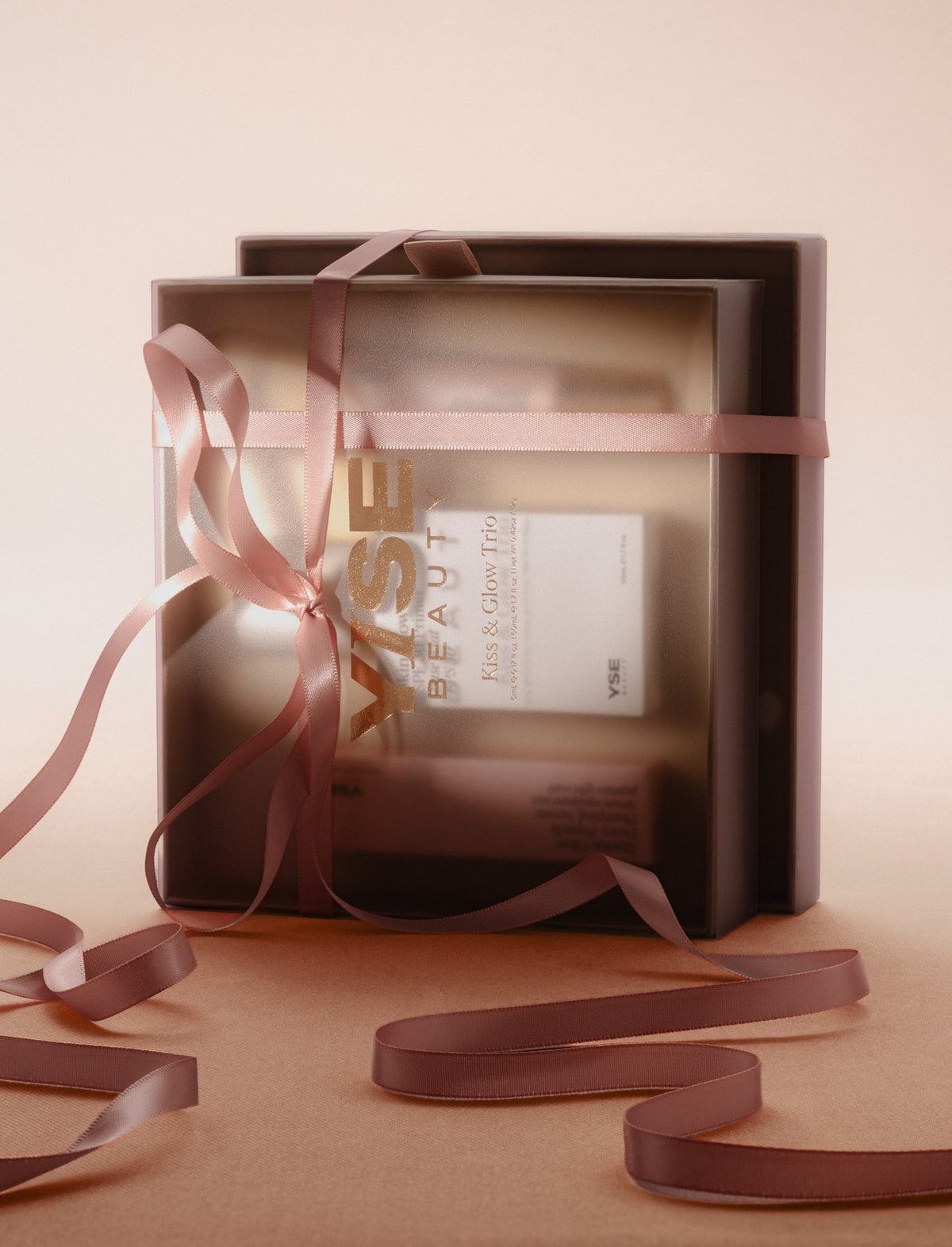 Kiss & Glow Trio gift box in a sheer sleeve, tied with a dusty-pink satin ribbon