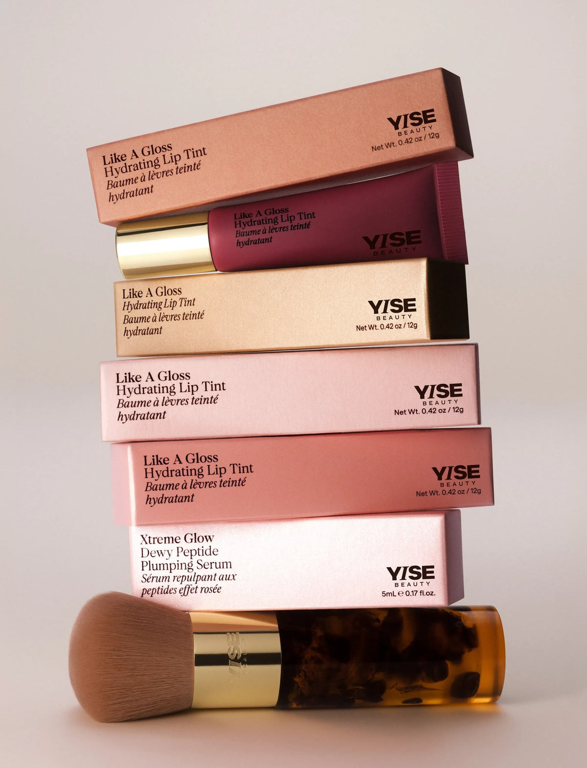 Like a Gloss Hydrating Lip Tint boxes stacked on an Xtreme Glow serum box, with a makeup brush in front