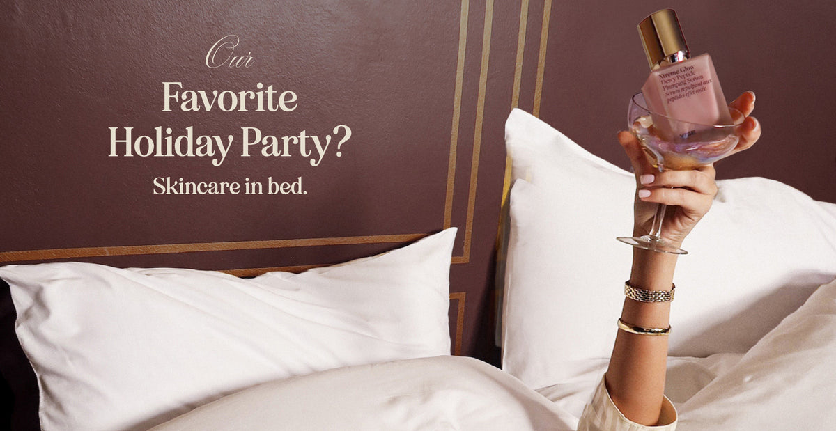 Our favorite holiday party? Skincare in bed. A hand rises from white hotel pillows holding a coupe glass and a bottle of Xtreme Glow serum.