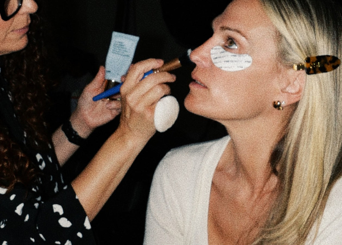 A makeup artist applies moisturizer under Molly Sims' eye backstage.